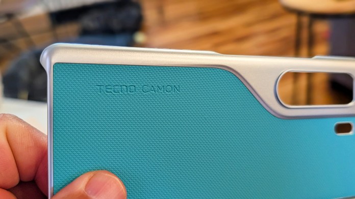 Close-up view of a Tecno Camon phone case featuring a textured turquoise design and silver edges, with 'TECNO CAMON' embossed.