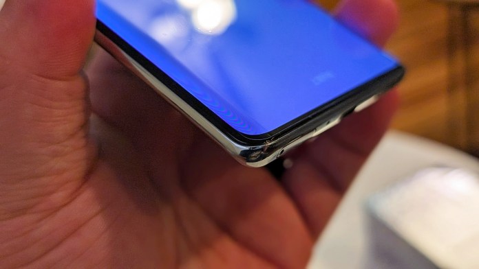 Close-up view of a person's hand holding the side of a smartphone with a blue display, showcasing its sleek design and edges.