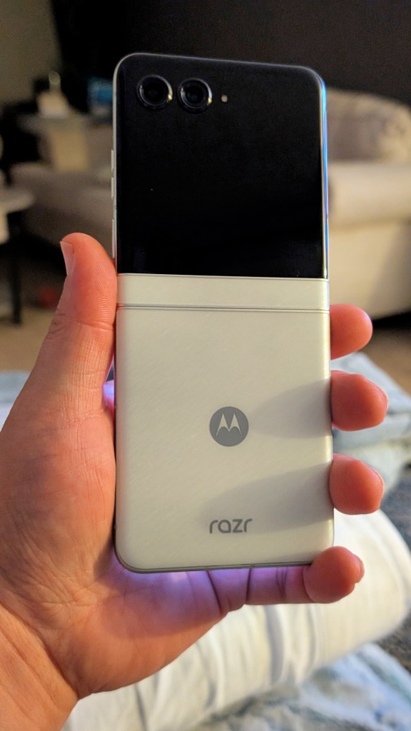A person holding a Motorola Razr smartphone in a compact, folded position, showcasing its sleek design with a glossy surface and two rear cameras.