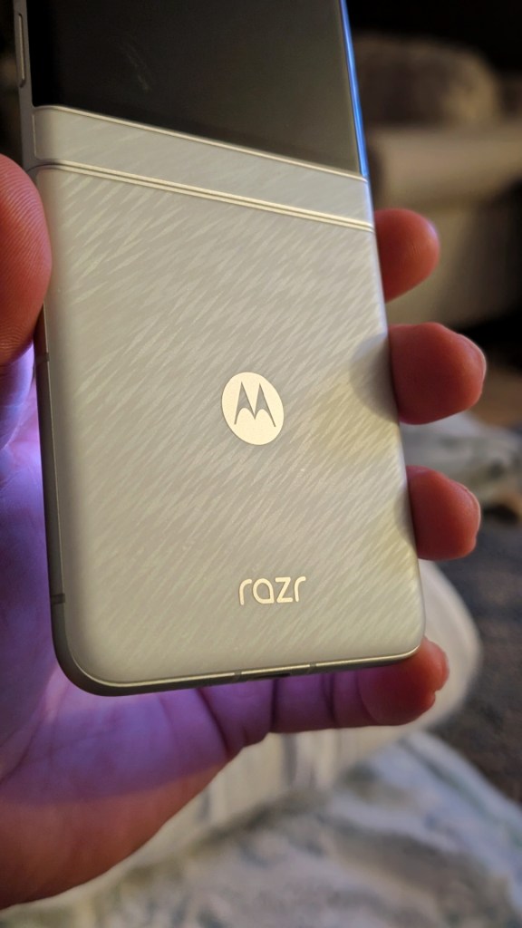 Close-up of a person's hand holding a Motorola Razr smartphone, showcasing its sleek silver design and logo.