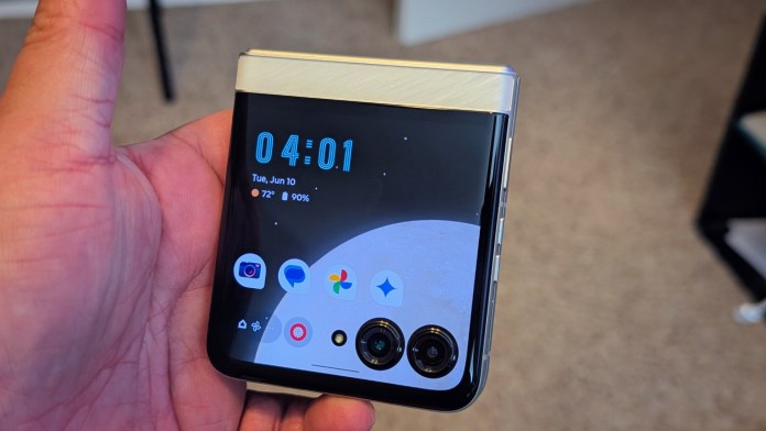 A person holding a Motorola Razr 2025 flip phone, showing the external display with time and app icons.