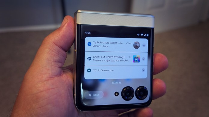 A close-up view of the Motorola Razr 2025 held in a hand, featuring its external display showing notifications and the time.