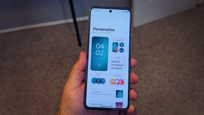 A person holding a Motorola Razr smartphone displaying the personalization screen with options for colors, themes, fonts, and icon shapes.