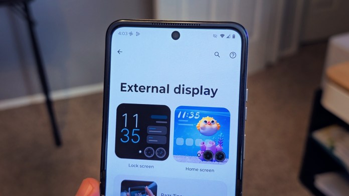 Close-up of a smartphone's external display showing time and app options, with a blurred background.