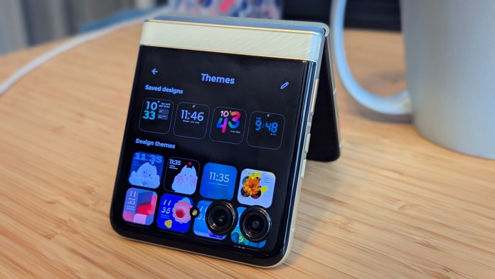 A Motorola Razr 2025 flip phone displayed on a wooden surface, showcasing its external screen with various app themes, time, and a camera module.