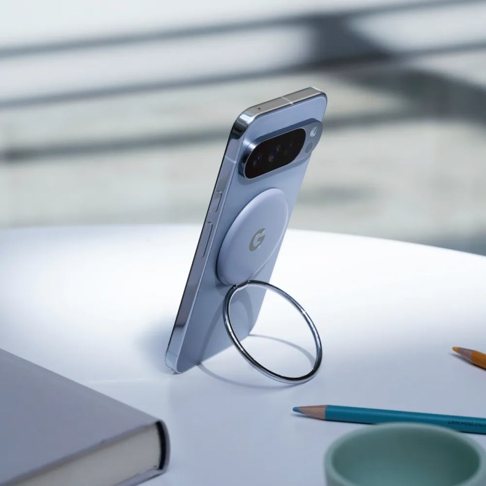 A Google Pixel phone propped up on a table using a circular ring stand, with a notebook and colorful stationery in the foreground.