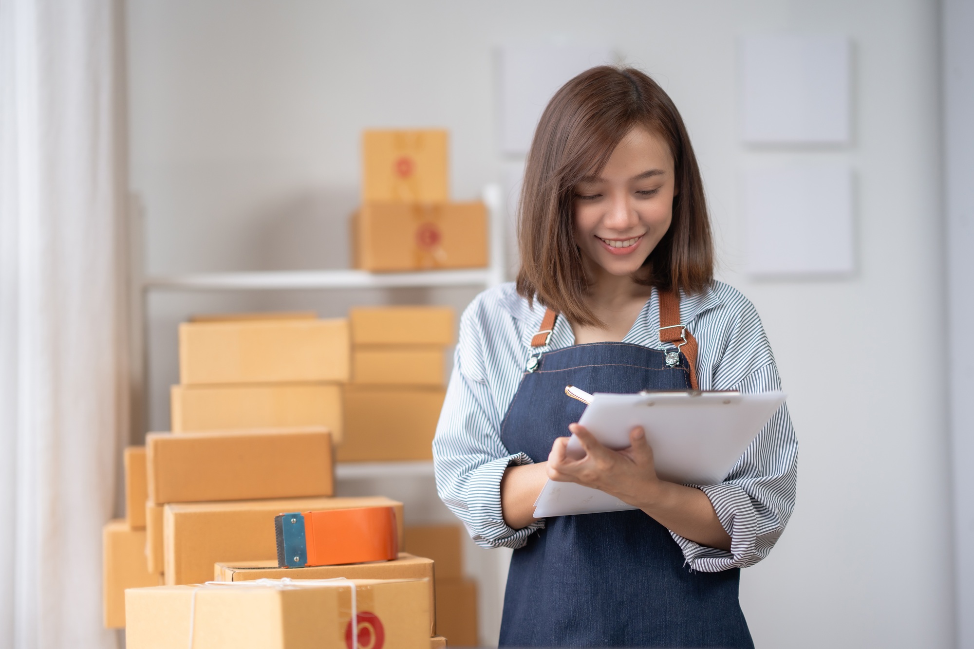 Smiling woman in apron checking package inventory with clipboard