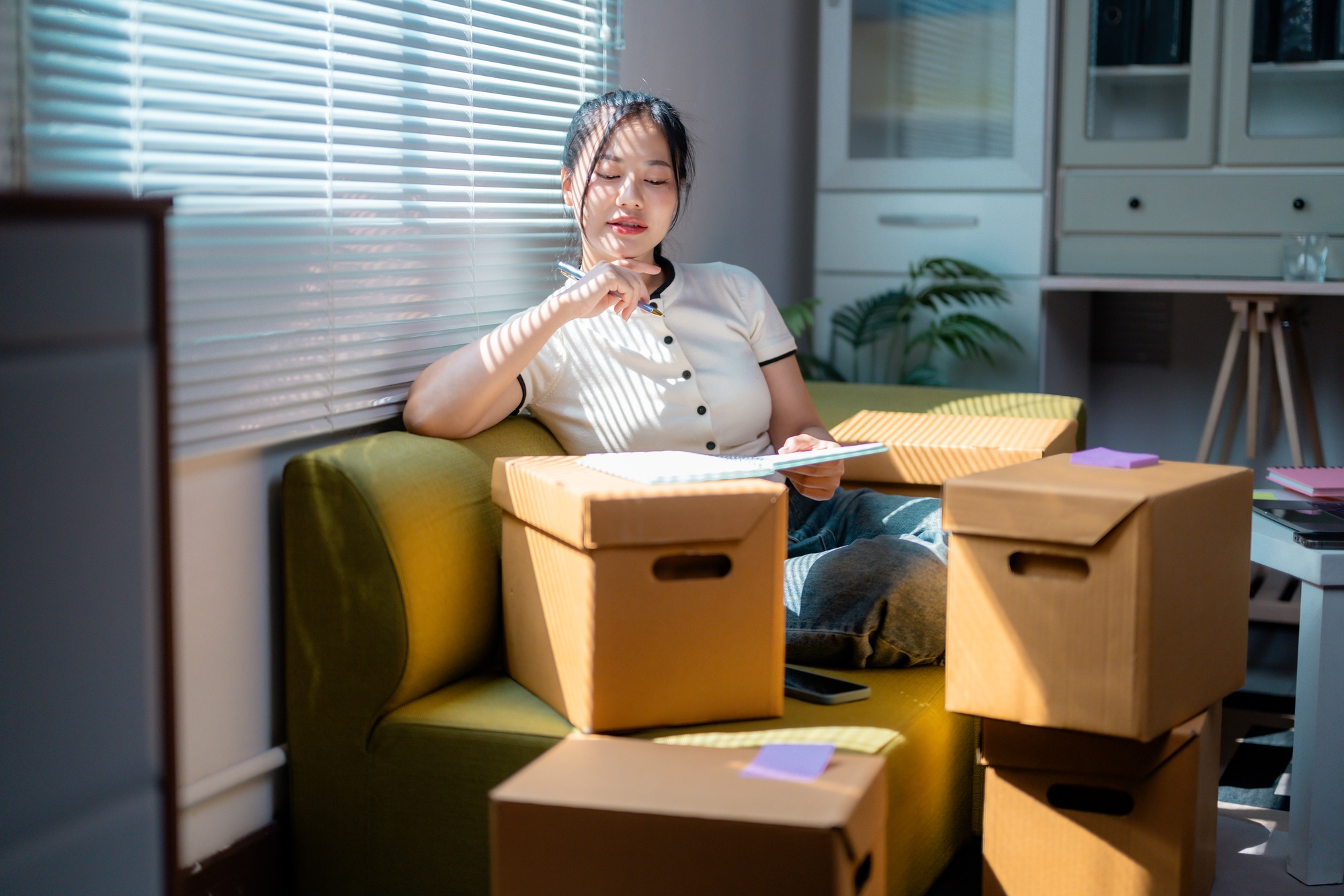 Asian Female Entrepreneur Checking Inventory in Home Office with Cardboard Boxes