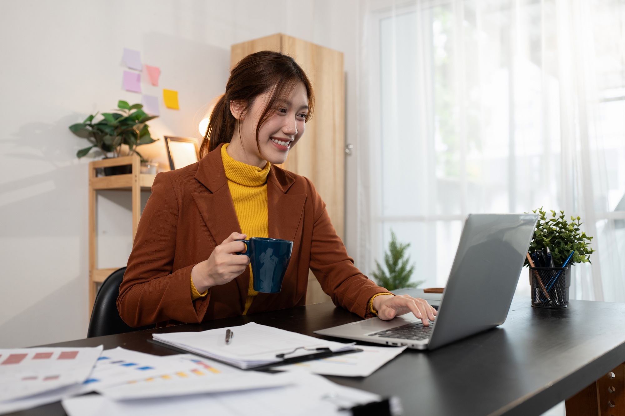Small business owner managing documents, laptop, and online success in a modern workspace.
