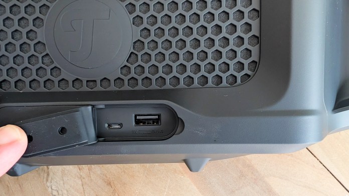 Close-up of the ports on the Fender x Teufel ROCKSTER CROSS Bluetooth speaker, showcasing a USB port and a charging input, with a textured surface in the background.