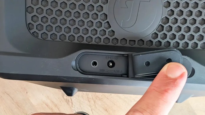 Close-up view of the connection ports on the Fender x Teufel ROCKSTER CROSS Bluetooth speaker, featuring a protective cover and a finger pointing at the input options.