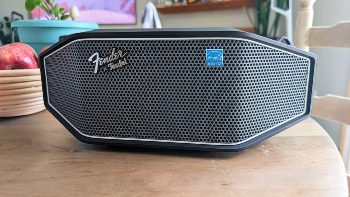 Fender x Teufel ROCKSTER CROSS Bluetooth speaker with steel mesh grille and iconic branding on a wooden table next to an apple bowl.