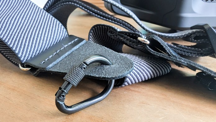 Close-up of a Fender guitar strap featuring a metal clip and contrasting striped design, laid on a wooden surface.