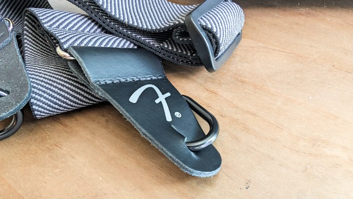 Close-up of a Fender guitar strap, featuring a black leather end tag with a logo and a striped fabric design.